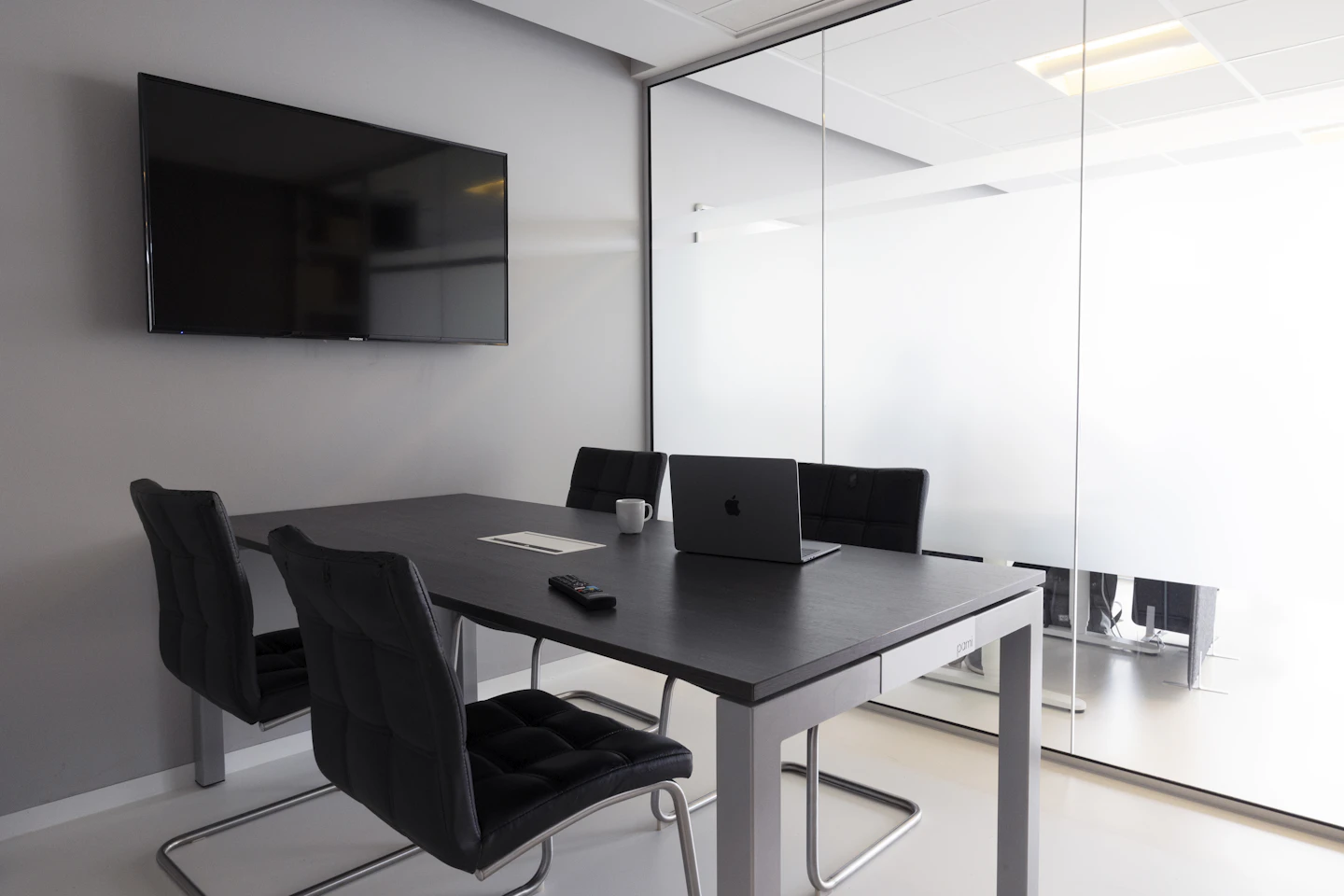 Petite salle de réunion avec un ordinateur portable sur la table et un écran mural éteint.